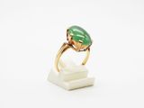 une bague en jade vert et or posée sur un bloc de marbre blanc