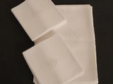 trois serviettes blanches ornées de monogrammes, posées sur une table