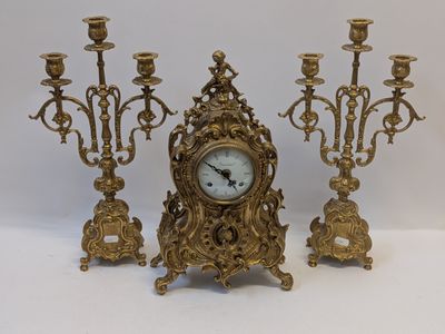 a gold clock sitting next to three candles on a table