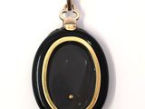 an oval black and gold pendant with a black stone in the center