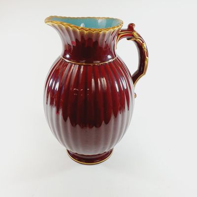 a red and blue vase with a gold handle on a white surface