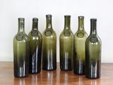 Six bouteilles de vin vertes sont alignées sur une table en bois