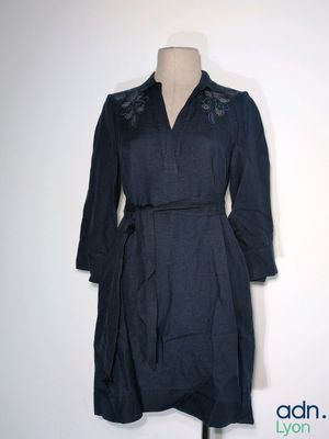 La robe est en lin bleu foncé et présente une ceinture à la taille.