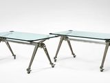une paire de tables en verre avec des pieds en métal et des roulettes