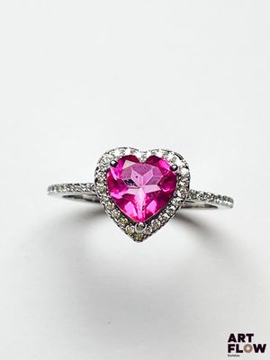 un gros plan d'une bague rose en forme de cœur posée sur une surface blanche