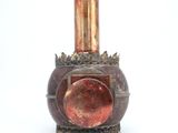 un vase rouge surmonté d'un couvercle doré, posé sur une surface blanche