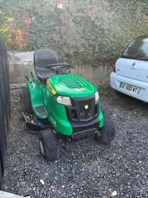 une tondeuse à gazon verte garée à côté d'une voiture blanche
