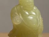 a green jade statue of a smiling buddha on a table