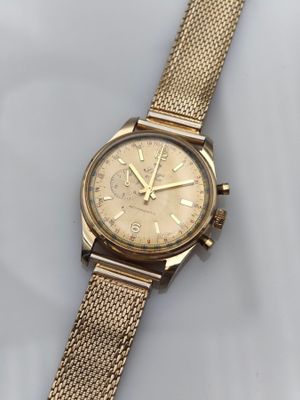 gros plan d'une montre en or sur une surface blanche