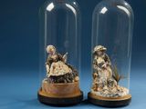 two glass cloches with figurines of people inside of them