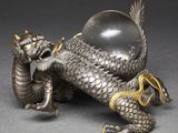 an antique silver dragon figurine with a glass ball on its back