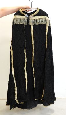Quelqu'un tient une veste noire ornée de franges dorées, suspendue à un cintre.