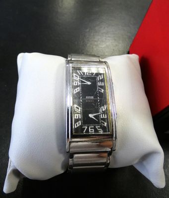 une montre argentée et noire posée sur une serviette blanche, sur une table noire
