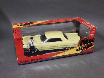 une petite voiture dans une boîte posée sur une surface grise, avec un homme debout à côté