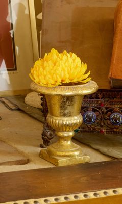 un vase en or contenant une fleur jaune, posé sur une table