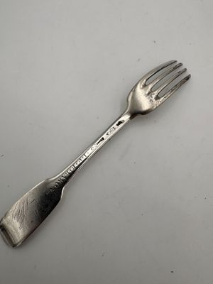 une fourchette plaquée argent posée sur une table blanche, sur fond blanc