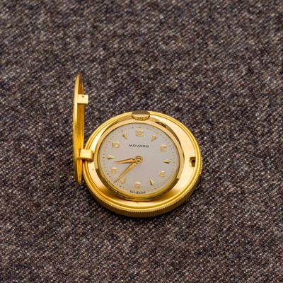 une petite montre de poche en or posée sur une surface marron