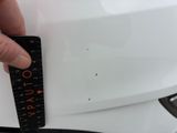 a hand holding a ruler that is on the hood of a white car