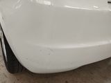 the rear end of a white car with a dent on it
