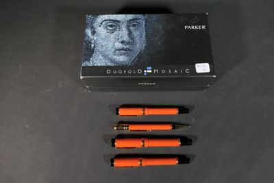 three orange pens sitting on top of a black table next to a box of ink