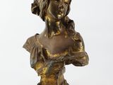 un buste en bronze représentant une femme vêtue d'une robe et tenant une fleur