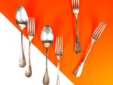 Plusieurs fourchettes et cuillères sont alignées sur un fond orange et blanc