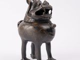 une vieille statue en bronze représentant un chien la gueule ouverte, sur fond blanc