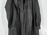 un vieux manteau noir suspendu à un cintre devant un mur blanc