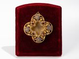 an image of a gold broochle on a red velvet box