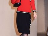 a woman that is walking down the runway in a red jacket and black skirt