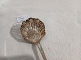 une cuillère en argent ornée d'un coquillage, posée sur une surface blanche