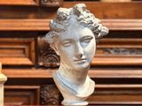une statue représentant une femme assise sur une table, à côté d'une bougie