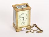 une petite horloge dorée avec une clé, posée sur une surface blanche