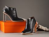 two pairs of black leather ankle boots sitting on top of an orange box