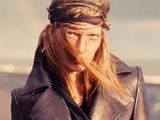 blond woman in black leather jacket and bandana standing on the beach