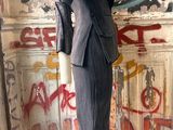 a mannequin in a suit on a stand in front of a graffiti covered wall