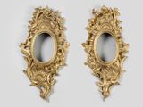une paire de miroirs ovales dorés accrochés à un mur blanc, sur fond blanc