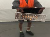 a man in an orange vest holding a ruler and a laptop