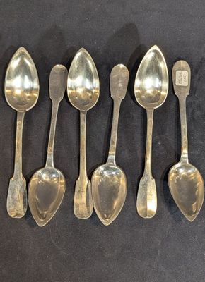 six cuillères en argent sont alignées sur une surface noire