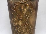 un vase doré orné de fleurs, posé sur une surface blanche