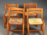 four wooden chairs with woven seats sit on a gray surface