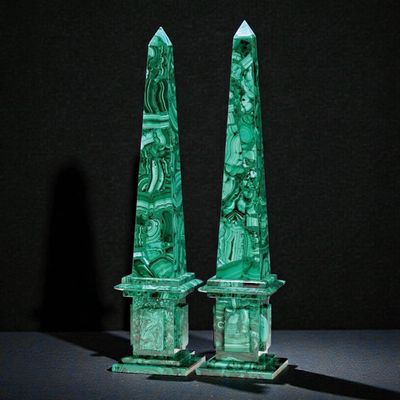 pair of green glass obelisks with carvings on them on a black surface