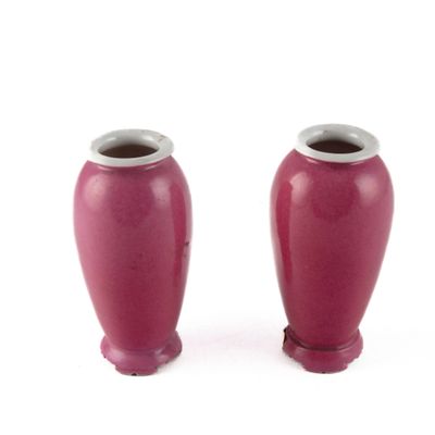 deux vases rouges posés l'un à côté de l'autre sur une surface blanche