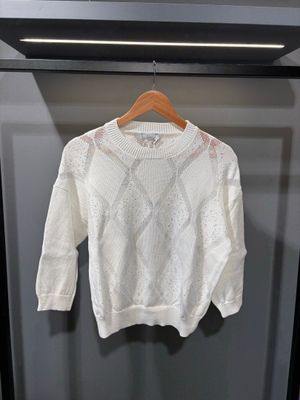 un pull blanc suspendu à un cintre devant un mur gris