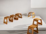 Plusieurs tabourets en bois sont alignés sur une surface blanche