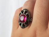 a close up of a person ' s hand holding a ring with a pink stone