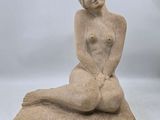 sculpture représentant une femme nue assise sur un coussin, sur fond blanc