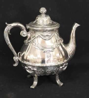 théière en métal argenté avec motif orné sur pied sur fond noir