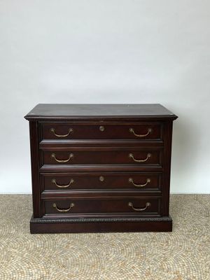 une petite commode posée sur un sol recouvert de moquette, devant un mur blanc