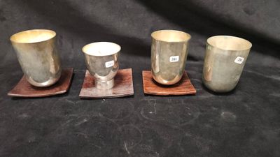 trois tasses en argent et leurs dessous de verre posés sur un tissu noir
